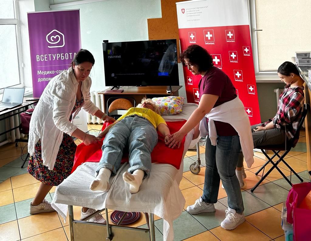 This is a photo from a training session on home care for people with limited mobility. A woman lies on a sofa, with two people standing next to her.