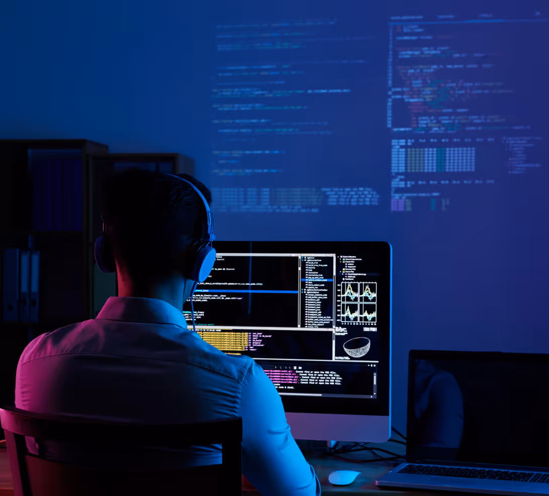 A man seated at a desk, focused on a computer screen in a well-lit office environment.