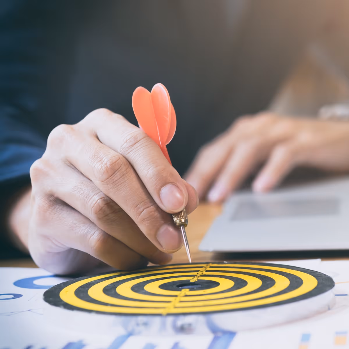 A person holds a dart in front of a dartboard, preparing to throw it at the target