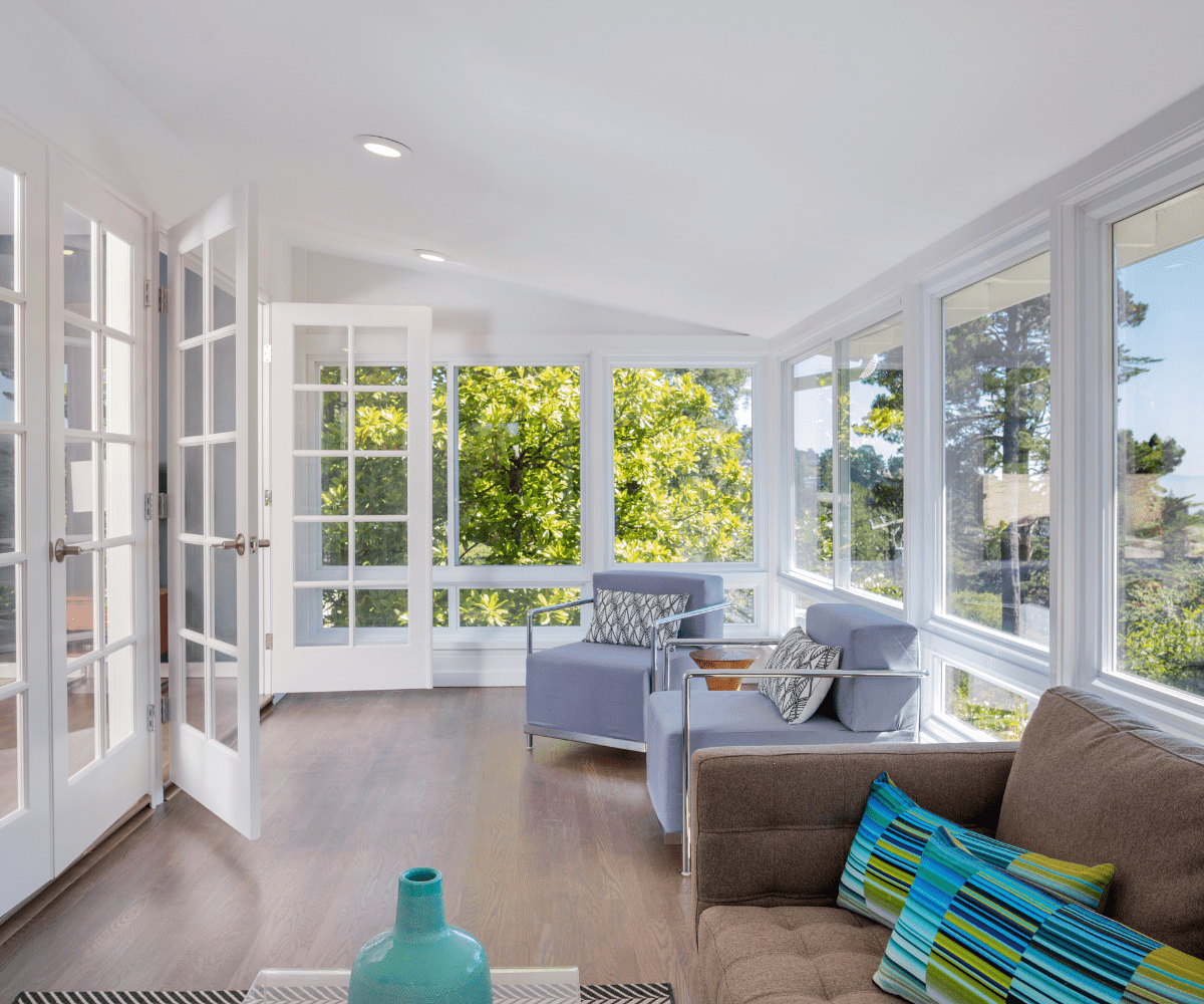 Finished lower-level living area with large windows, blue chairs, and a brown sofa after a basement remodel.