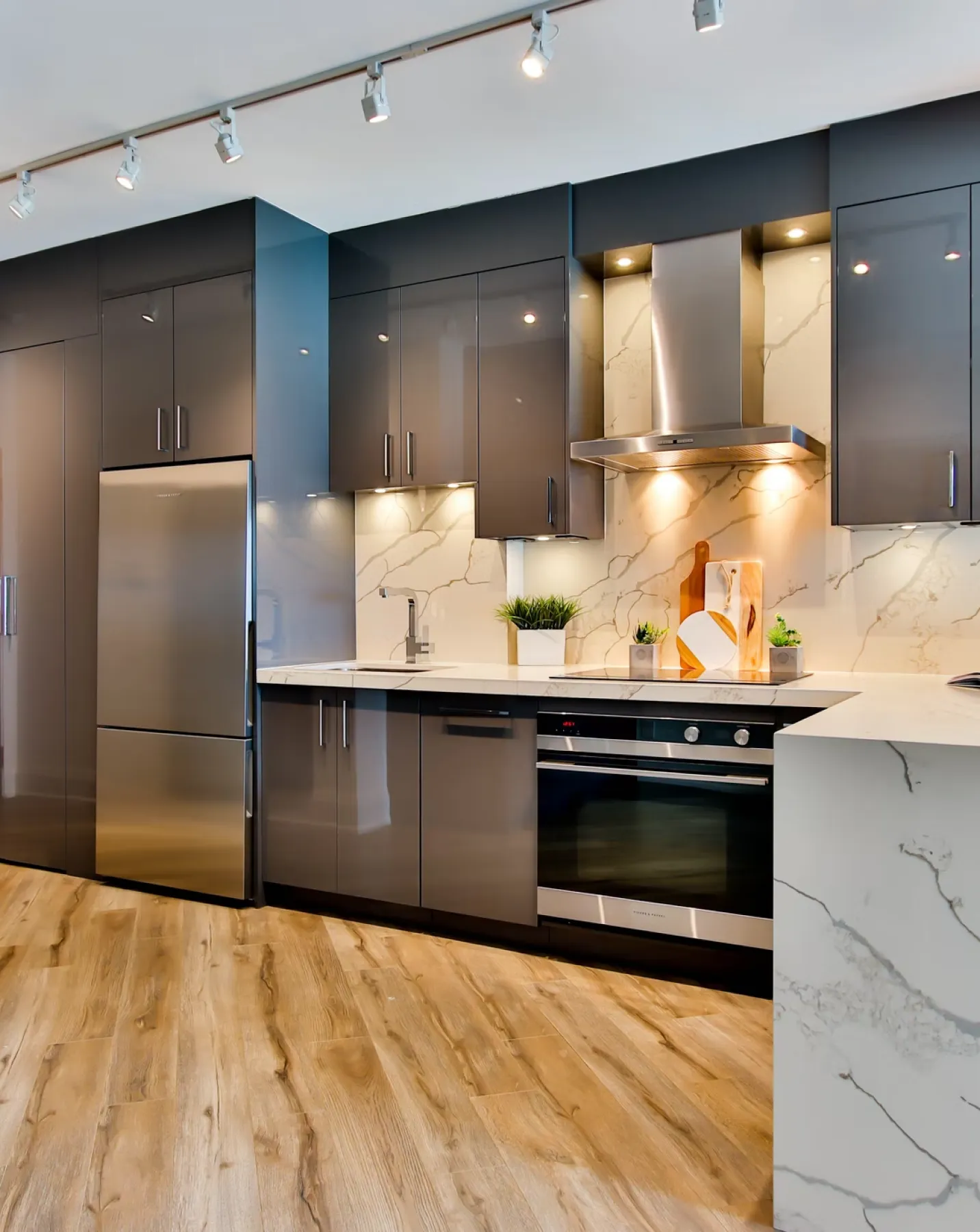 Modern kitchen with dark cabinets, stainless steel refrigerator, stove, marble countertops, and wood floor.