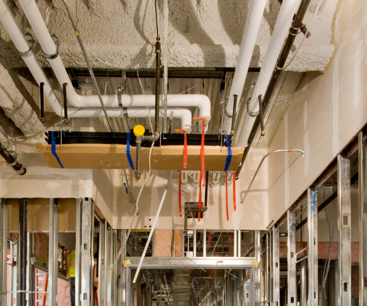 Open ceiling with pipes and conduits in an unfinished commercial space during a tenant improvement buildout.