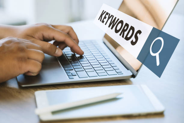 Person typing on laptop keyboard with keywords search bar and magnifying glass icon.