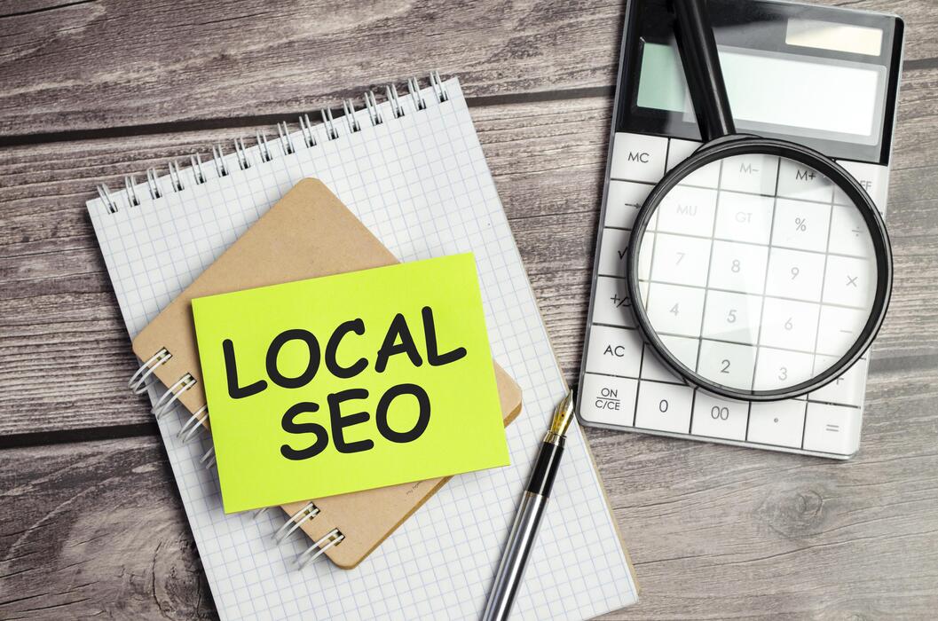 Local SEO written on green sticky note with notebook, magnifying glass and calculator on wooden desk.