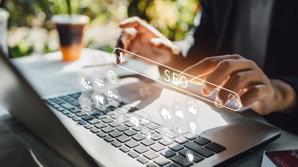 Person using laptop with SEO search bar and digital marketing icons overlay in bright workspace.