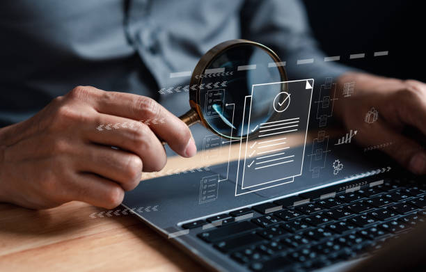 Person holding magnifying glass over laptop with digital document checklist and website audit icons.