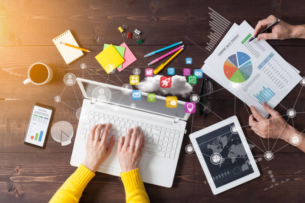 Digital marketing professional working on laptop with connected app icons, analytics charts, and mobile devices on a desk.