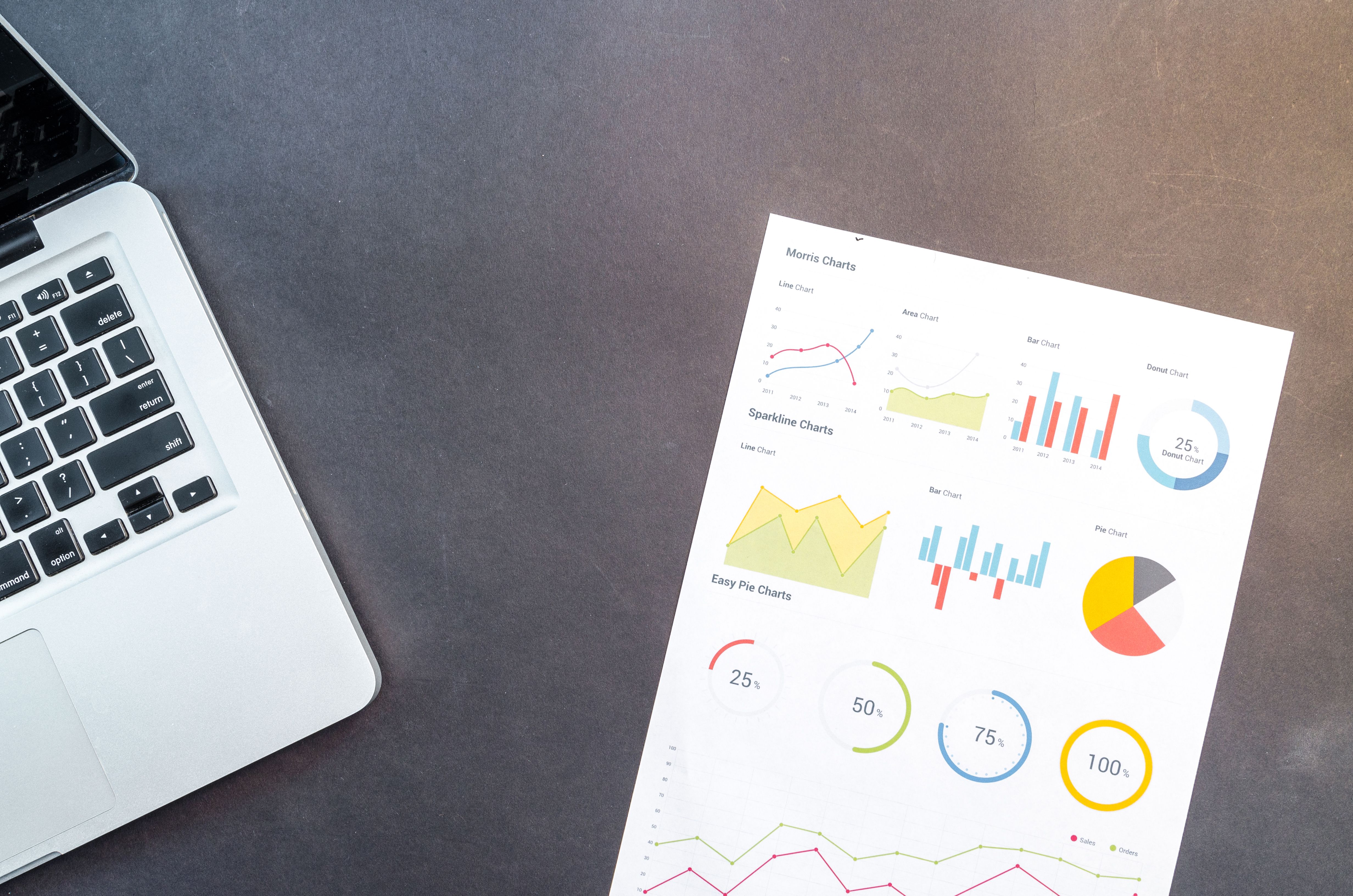 Marketing performance charts printed beside a laptop keyboard on a dark desk