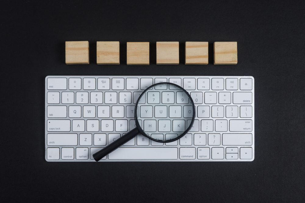 A magnifying glass placed on a white keyboard with building blocks on top of them on a black background.