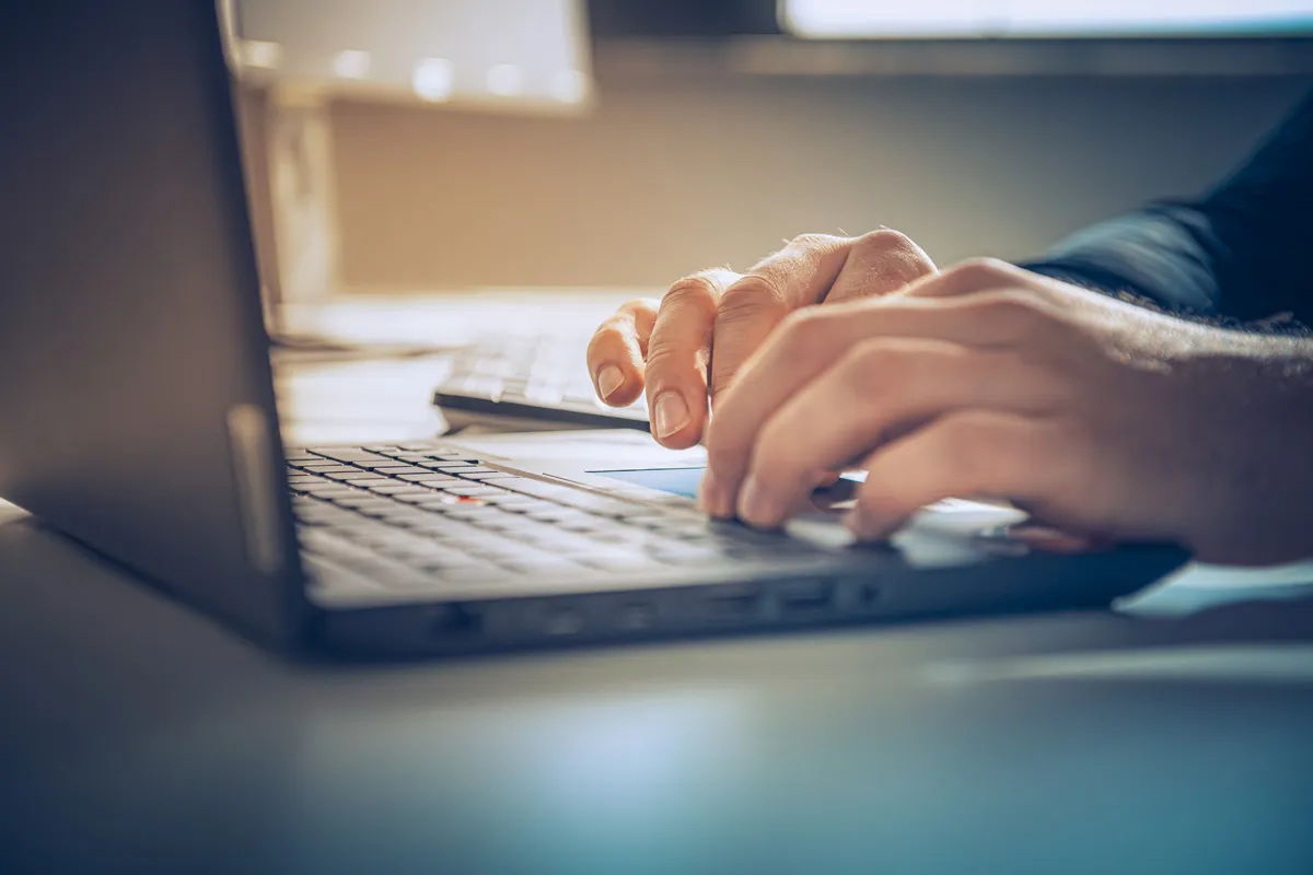 Hände, die auf einer Laptop-Tastatur tippen am Schreibtisch.