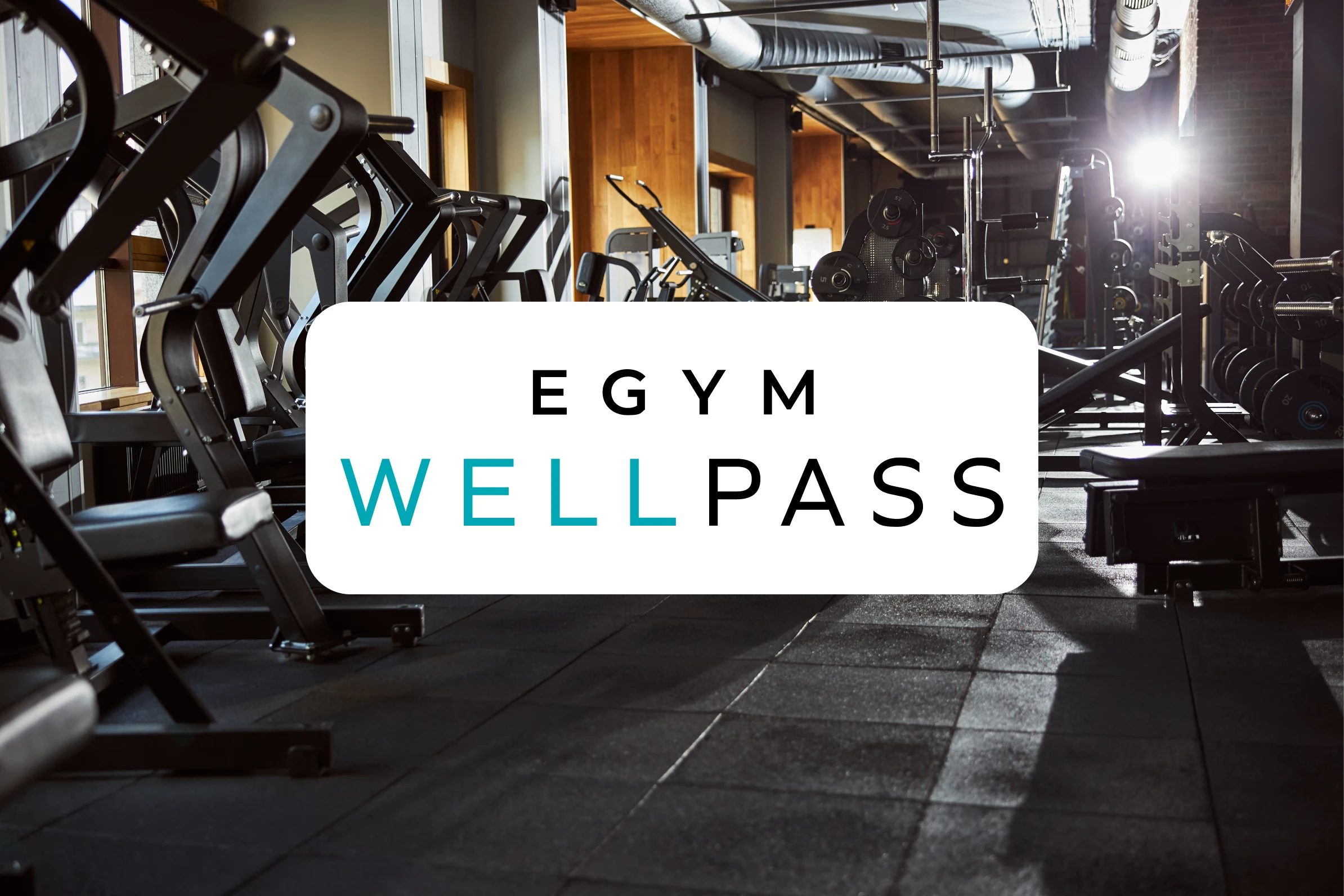 Fitnessstudio mit Krafttrainingsgeräten und große beleuchtete Fenster, im Vordergrund das Logo von EGYM Wellpass.