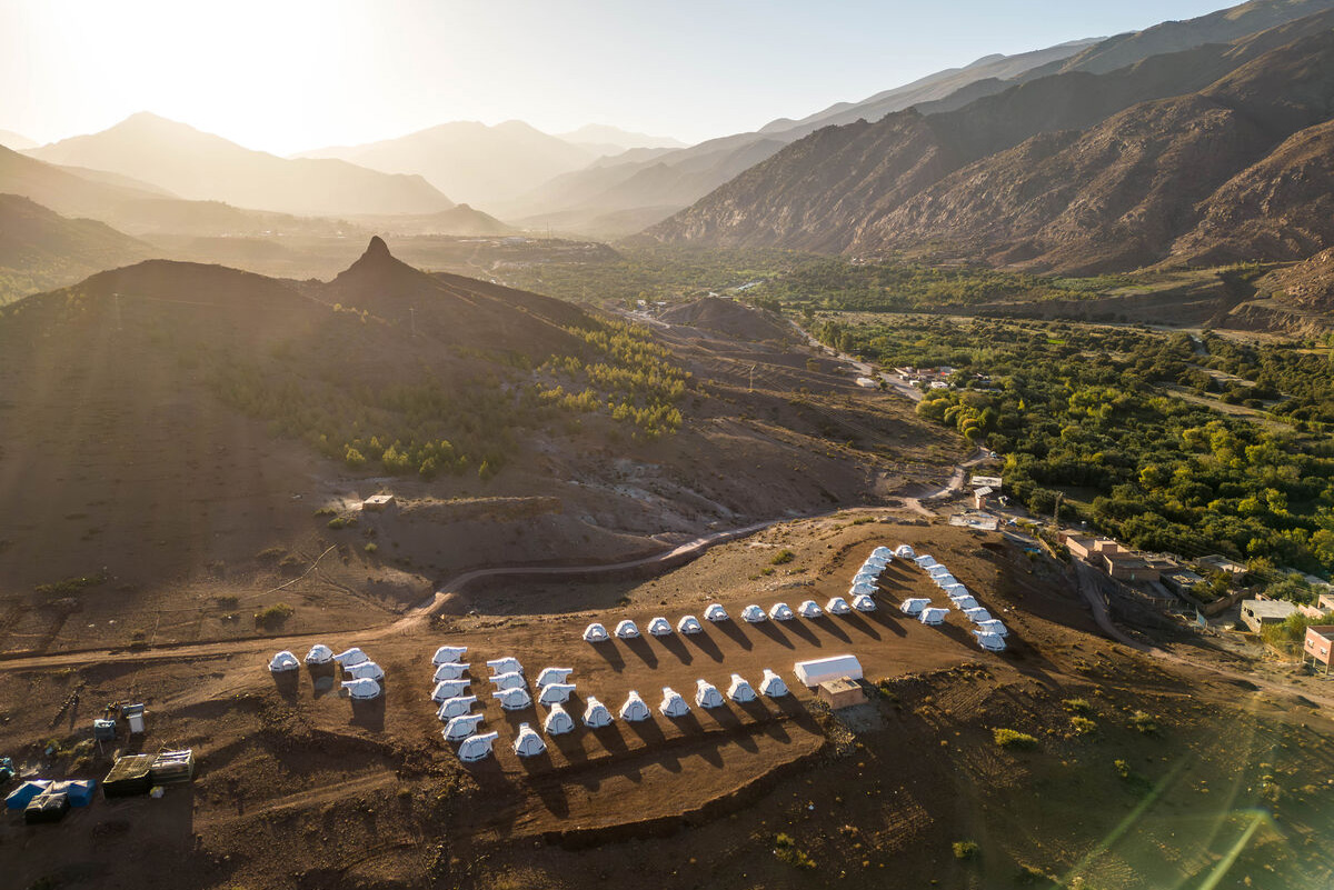 Weitläufige Landschaft mit provisorischen Unterkünften in bergiger Umgebung bei tiefstehender Sonne