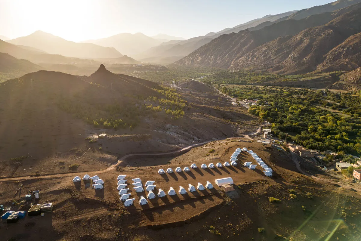 A vast landscape with makeshift shelters in a mountainous setting as the sun sets