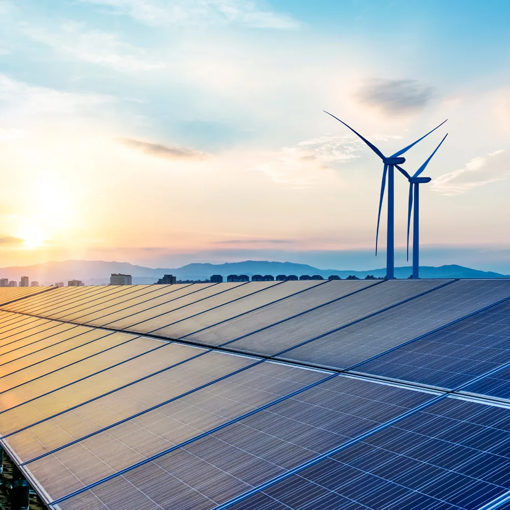 Solar panels and wind turbines generate renewable energy against a backdrop of mountains at sunset