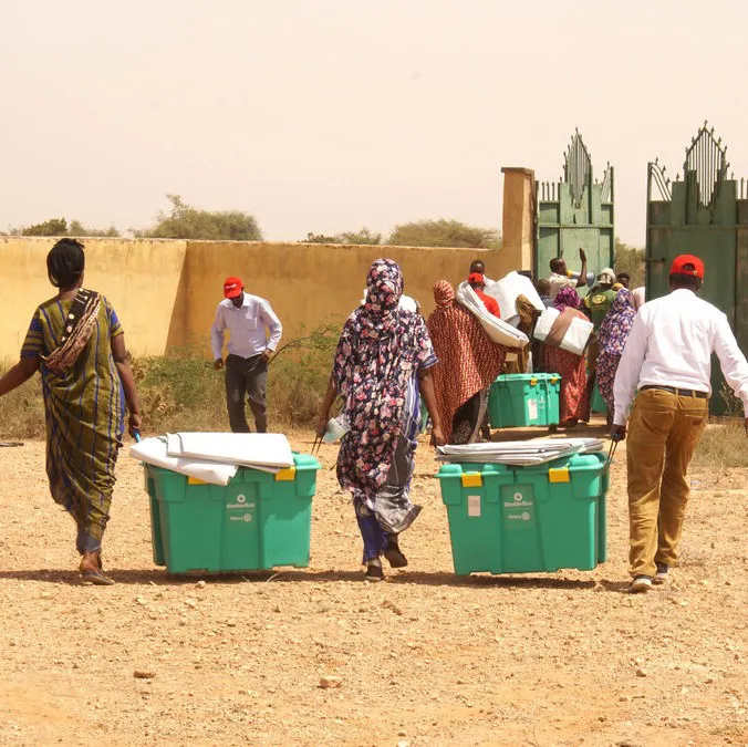 People are carrying green aid boxes to a collection point