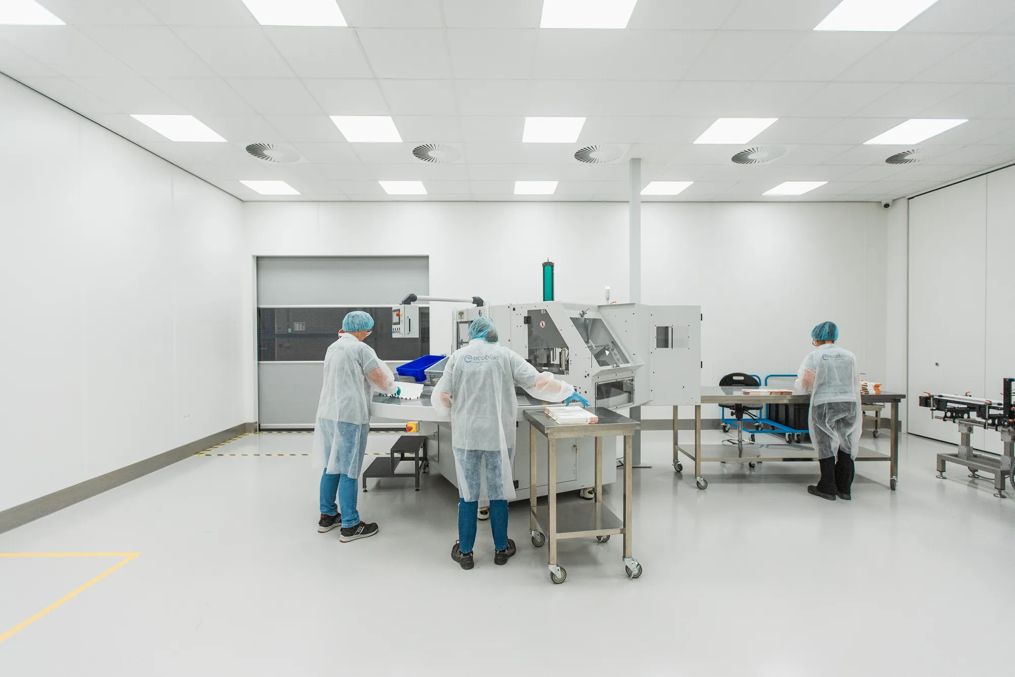 Operators in white coats and hairnets working at a packaging machine in the spacious GMP packaging room in Echt