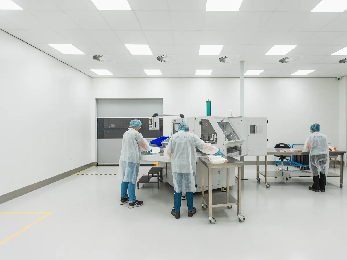 Operators in white coats working around a packaging machine in the spacious GMP packaging room