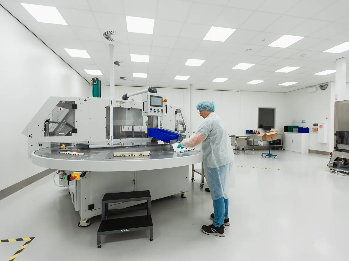 Operator loading a round-table packaging machine in a large white packaging room