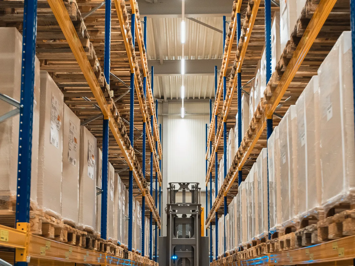 Wide view down a warehouse aisle between tall pallet racks full of packed goods