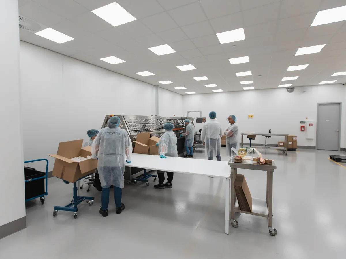 Staff in white coats and hairnets working around a long table in a large bright packaging hall