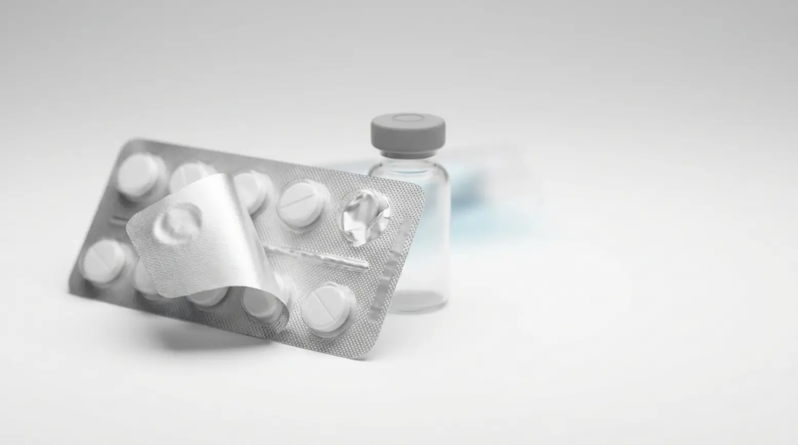 A sleek pharmaceutical blister pack and glass vial on a minimalistic, soft-toned background.