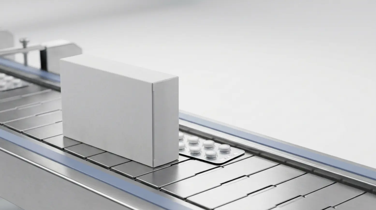 Neutral pharmaceutical carton on a stainless conveyor, paired with a silver blister pack.