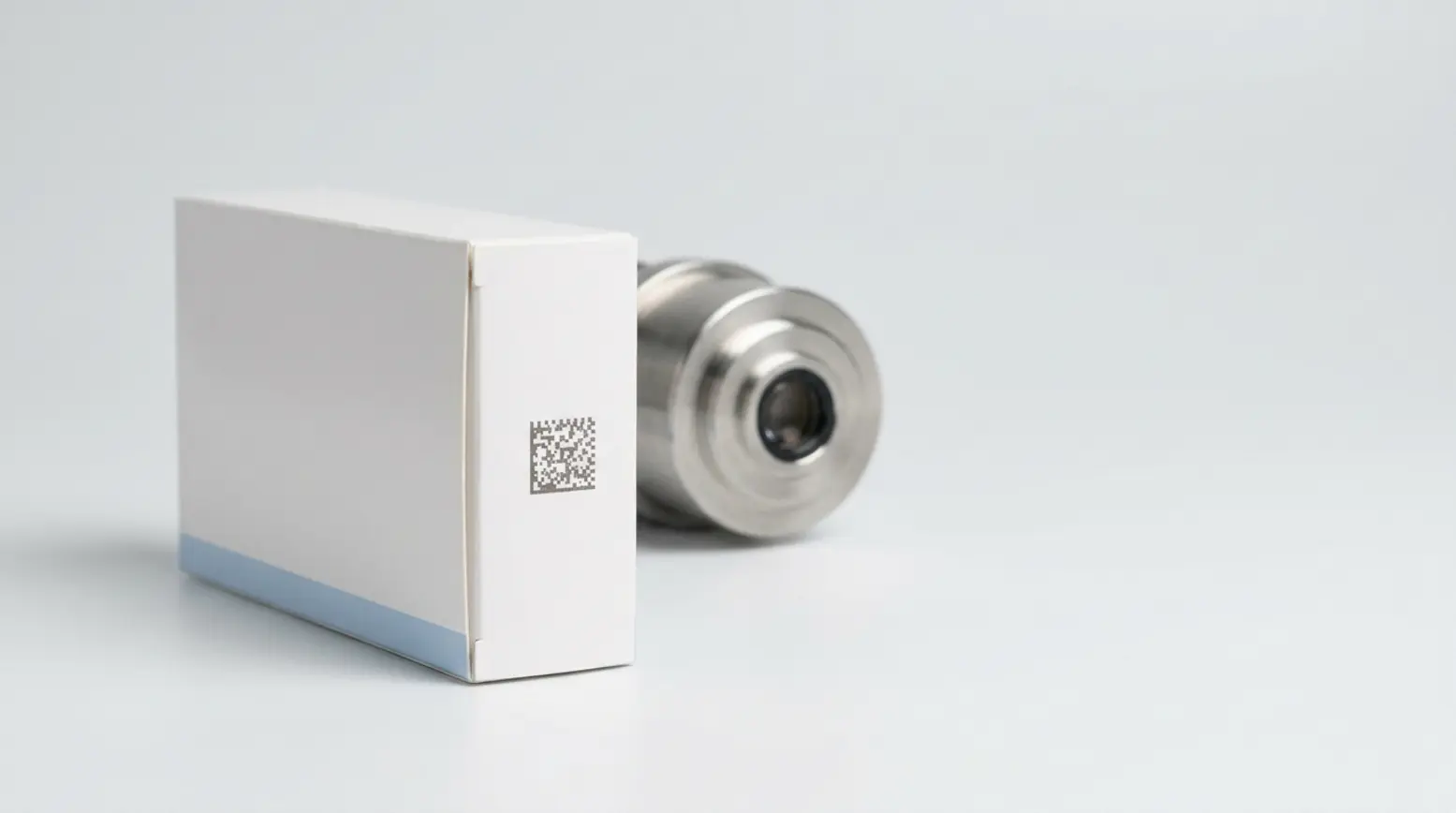 Pristine pharmaceutical carton with 2D code, soft focus camera behind, elegant studio setting.