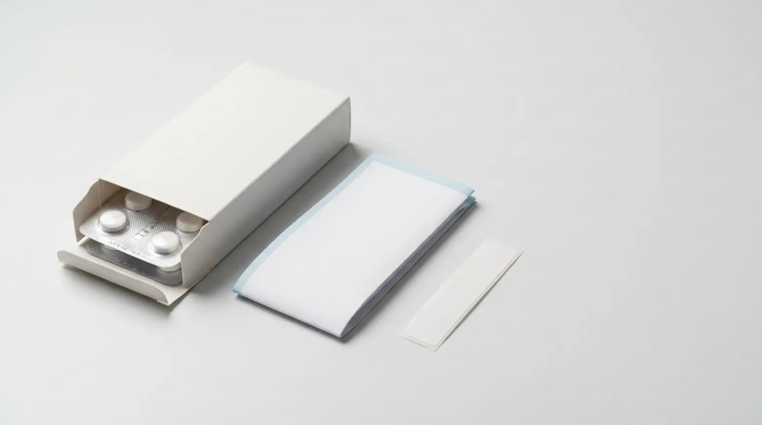 Pharmaceutical packaging with an open carton, blister pack, tablets, and a blank leaflet.