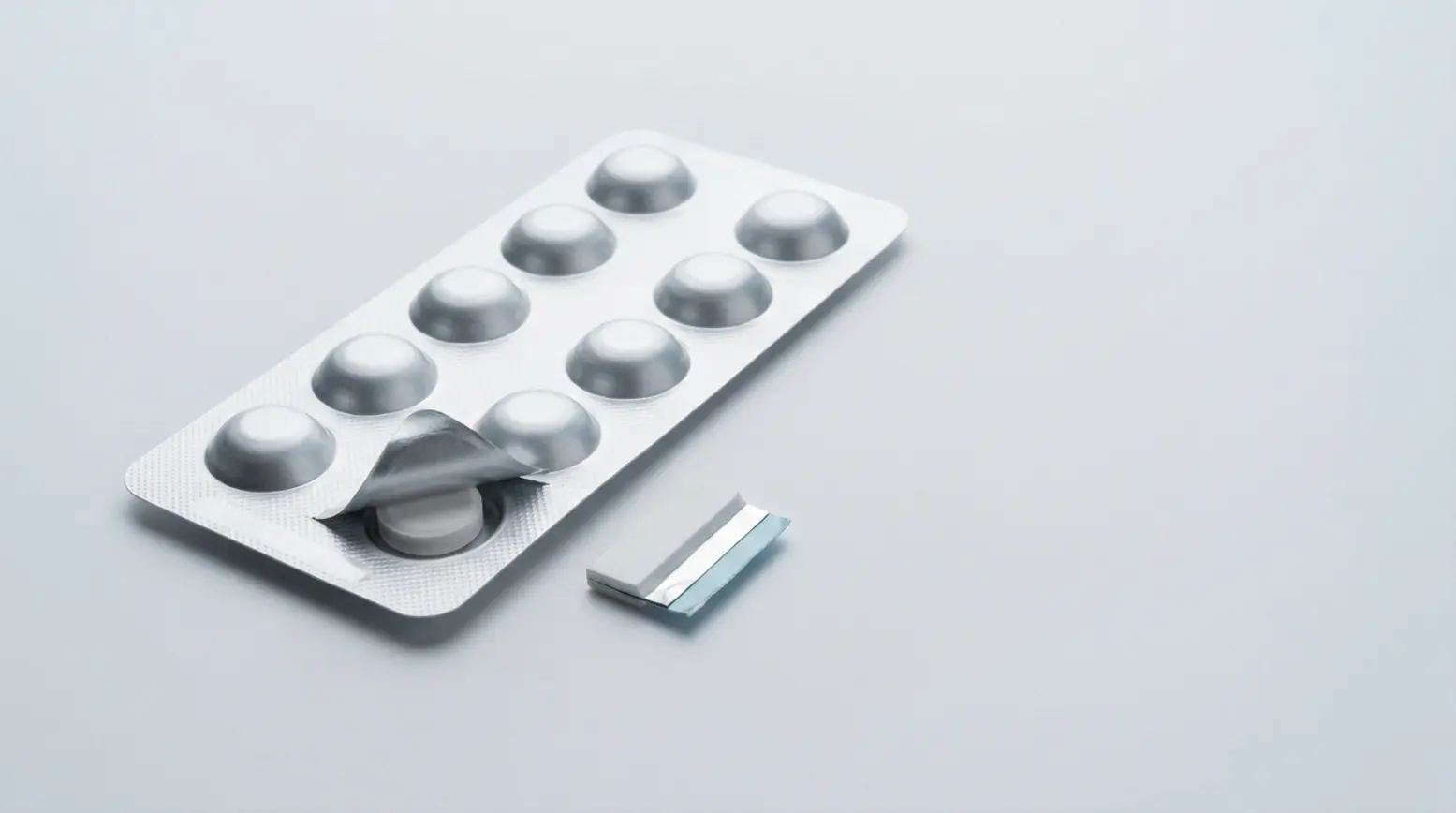 A sleek silver pharma blister pack revealing a white tablet against a light-grey backdrop.