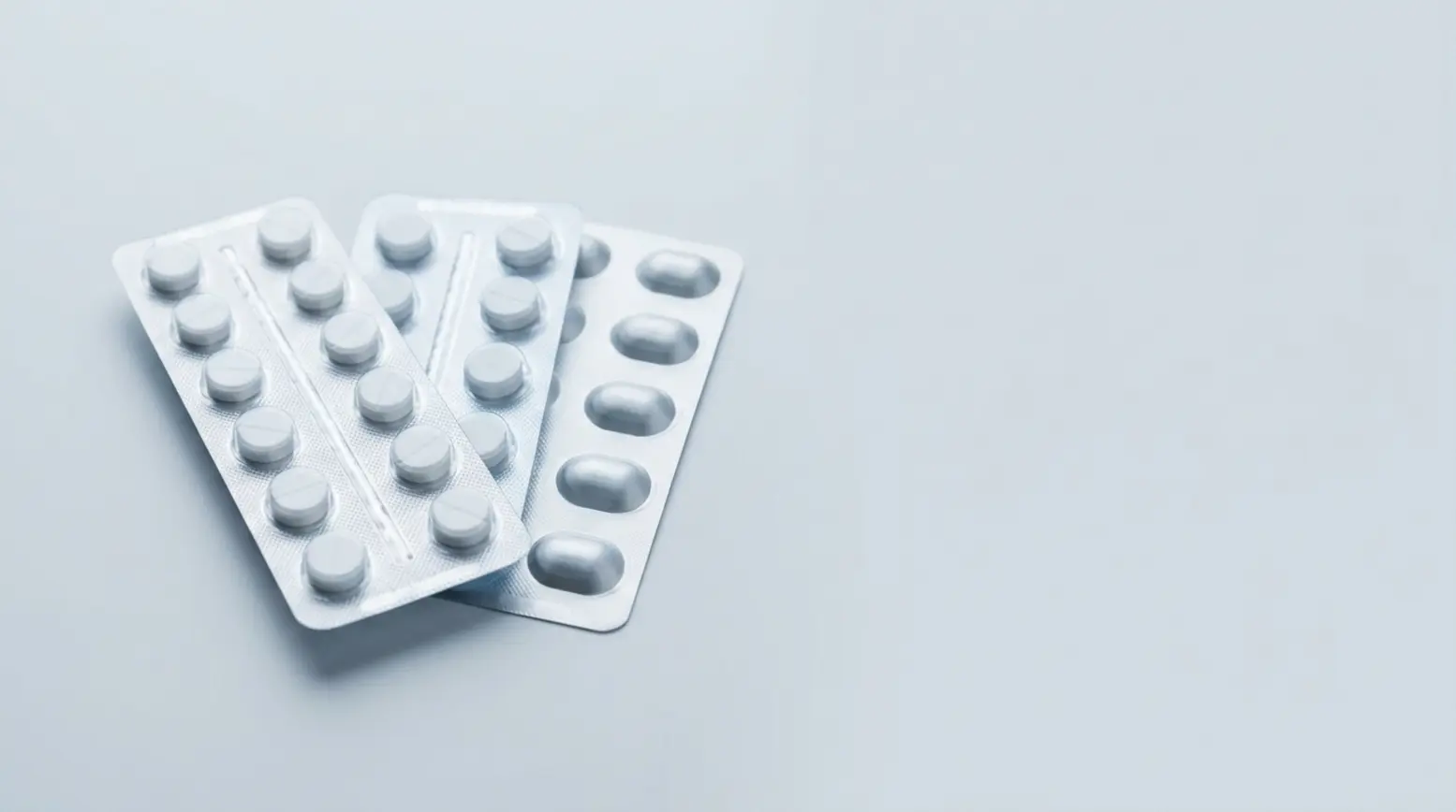 Three pharmaceutical blister packs displayed on a light-grey surface, showcasing details and textures.