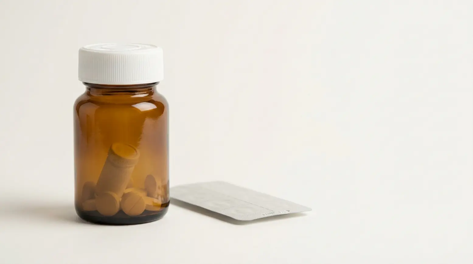 A polished photograph of an amber pharmaceutical bottle with a desiccant and tablets inside.