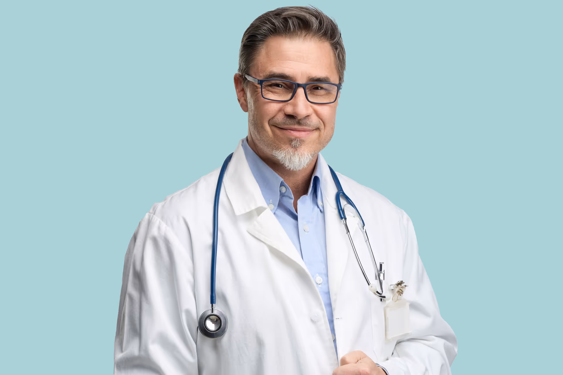 Doctor de mediana edad con gafas, bata blanca y estetoscopio, sonriendo sobre fondo celeste claro.
