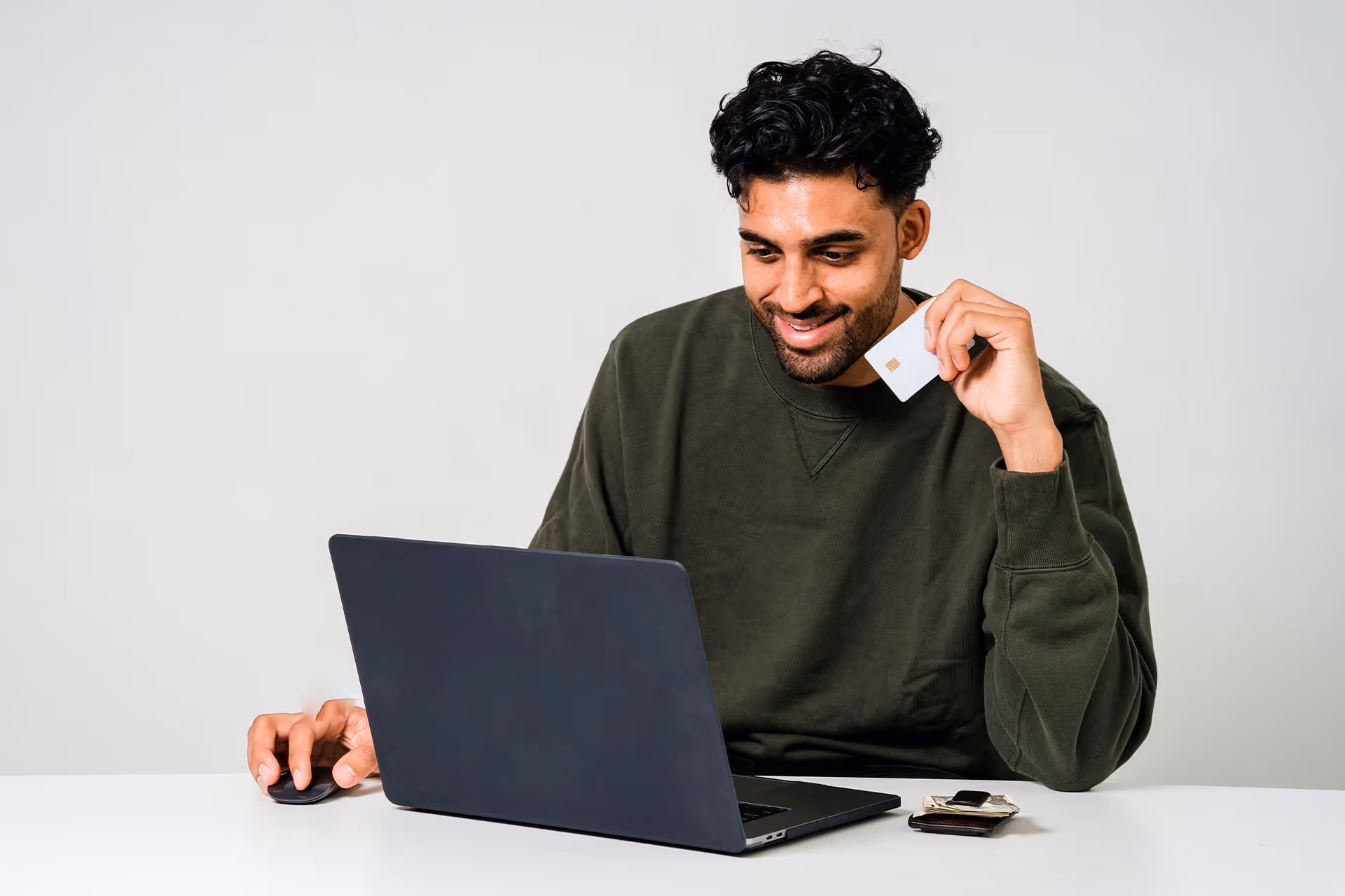 Hombre sonriendo mientras usa una laptop y sostiene una tarjeta, representando una compra o trámite en línea.