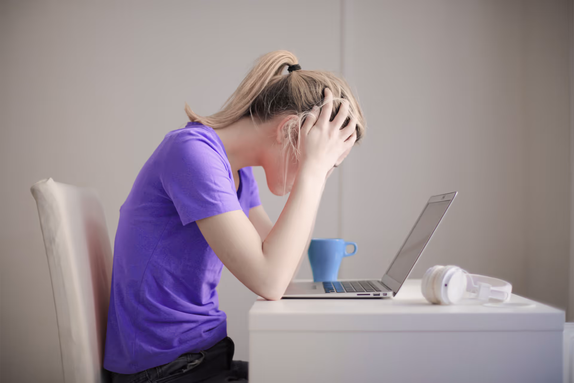 Mujer con expresión de frustración sosteniéndose la cabeza frente a su laptop, simbolizando estrés o problemas digitales.