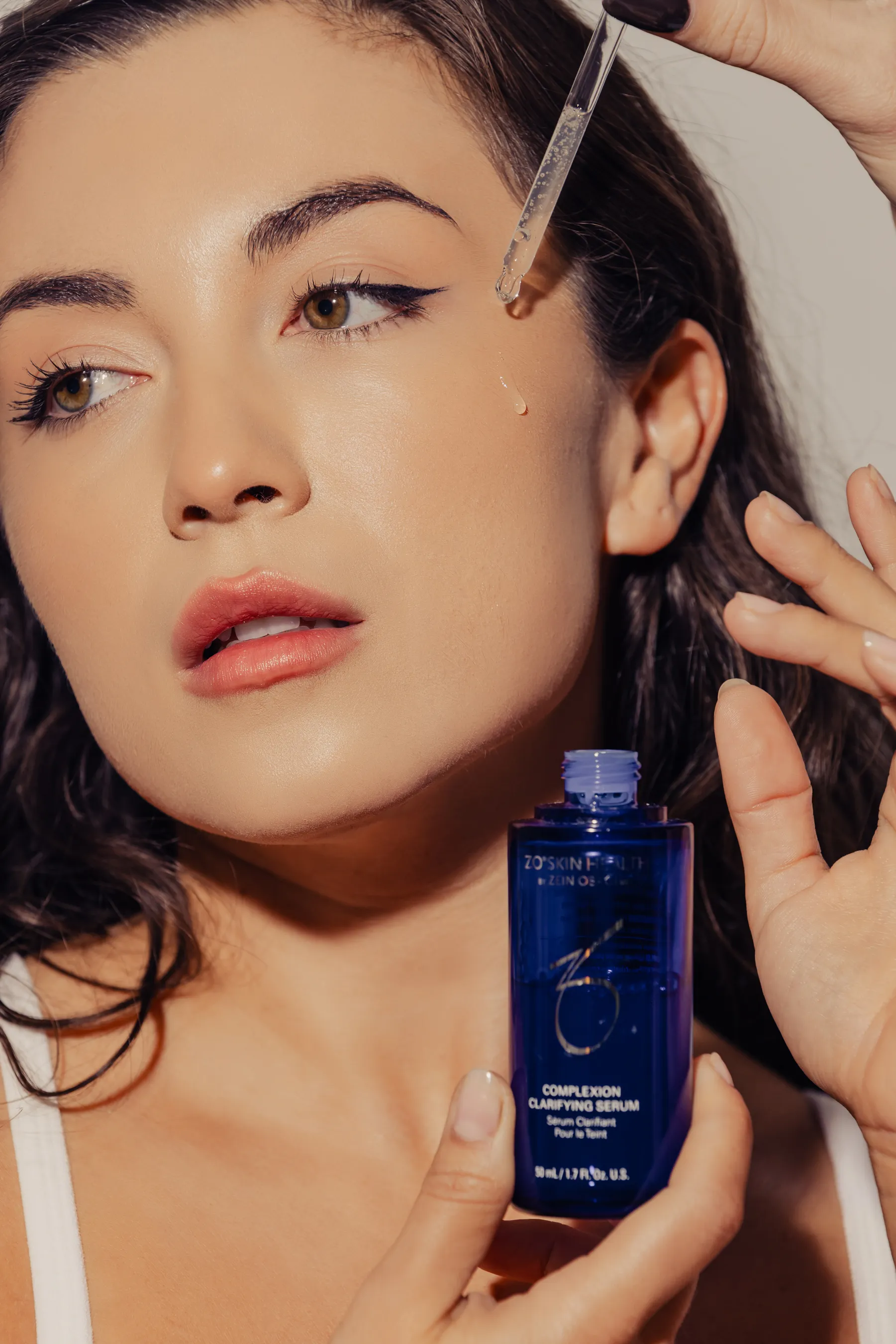 Woman applying a drop of Zo Skin Health Complexion Clarifying Serum to her cheek using a dropper.