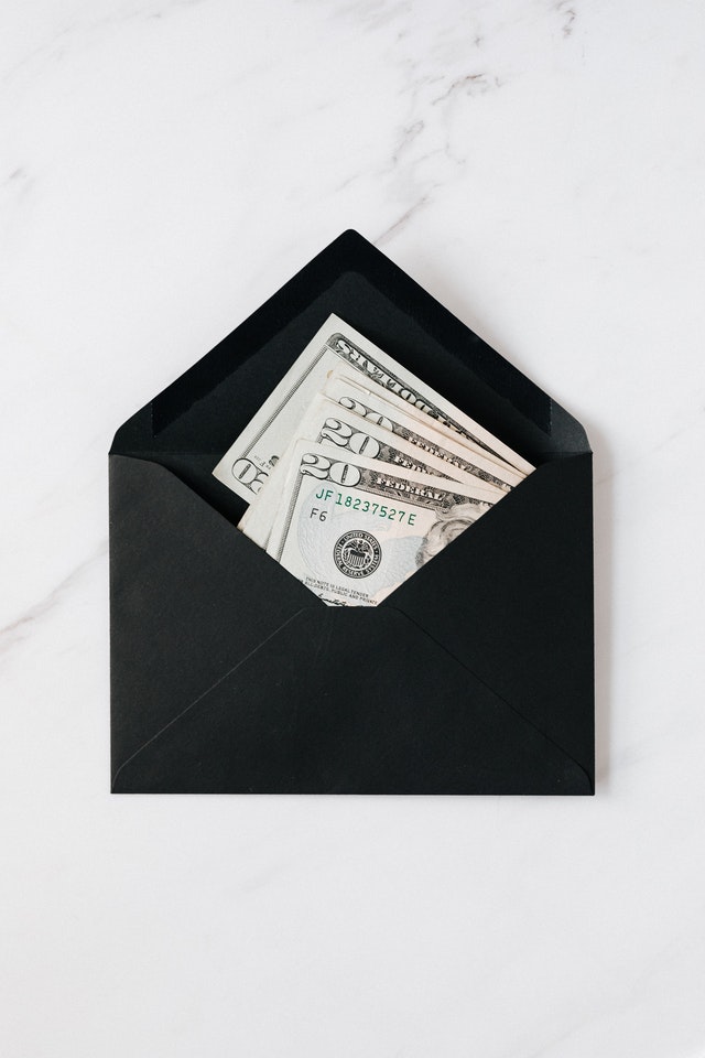A black envelope lying flat on a quartz table. The envelope is open and filled with several $20 bills.
