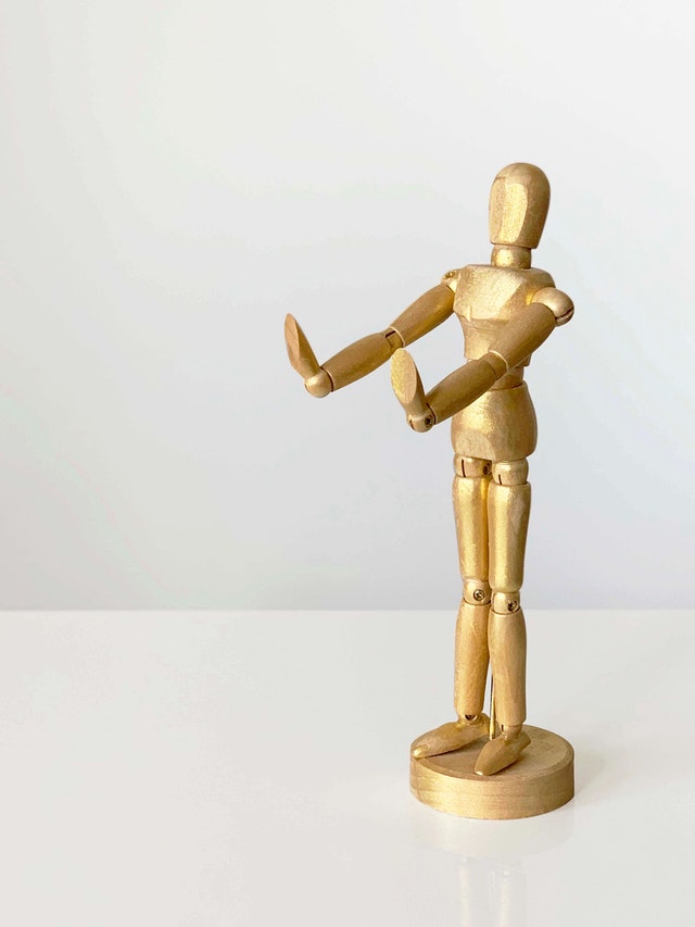 Small wooden mannequin with its arms outstretched making a "no" pose with its hands.