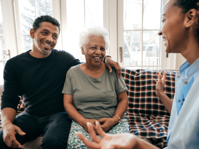 Illustration of a young caregiver supporting her older relative. Behind them are a Medicaid card, a shield with a check mark, and upward arrows that symbolize protection and positive progress.
