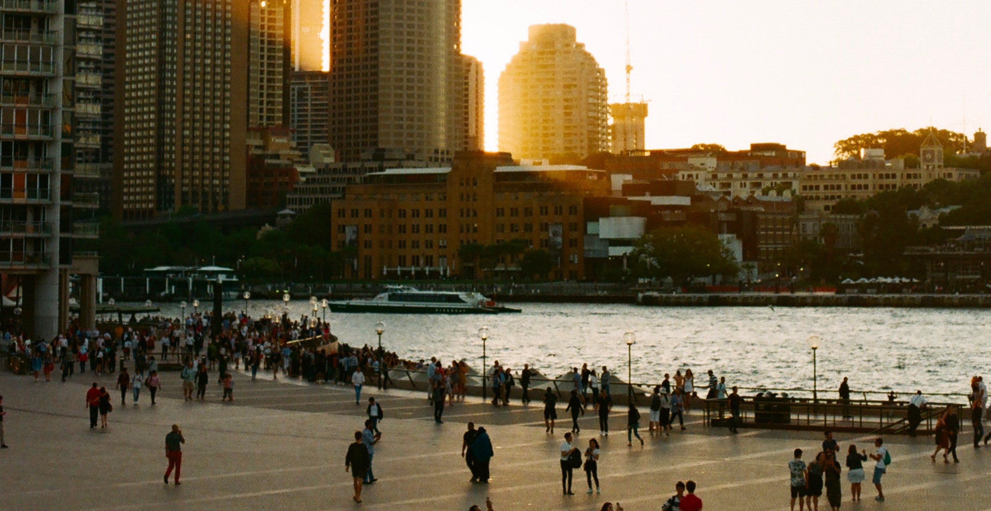 City waterfront at golden hour with crowds along the promenade