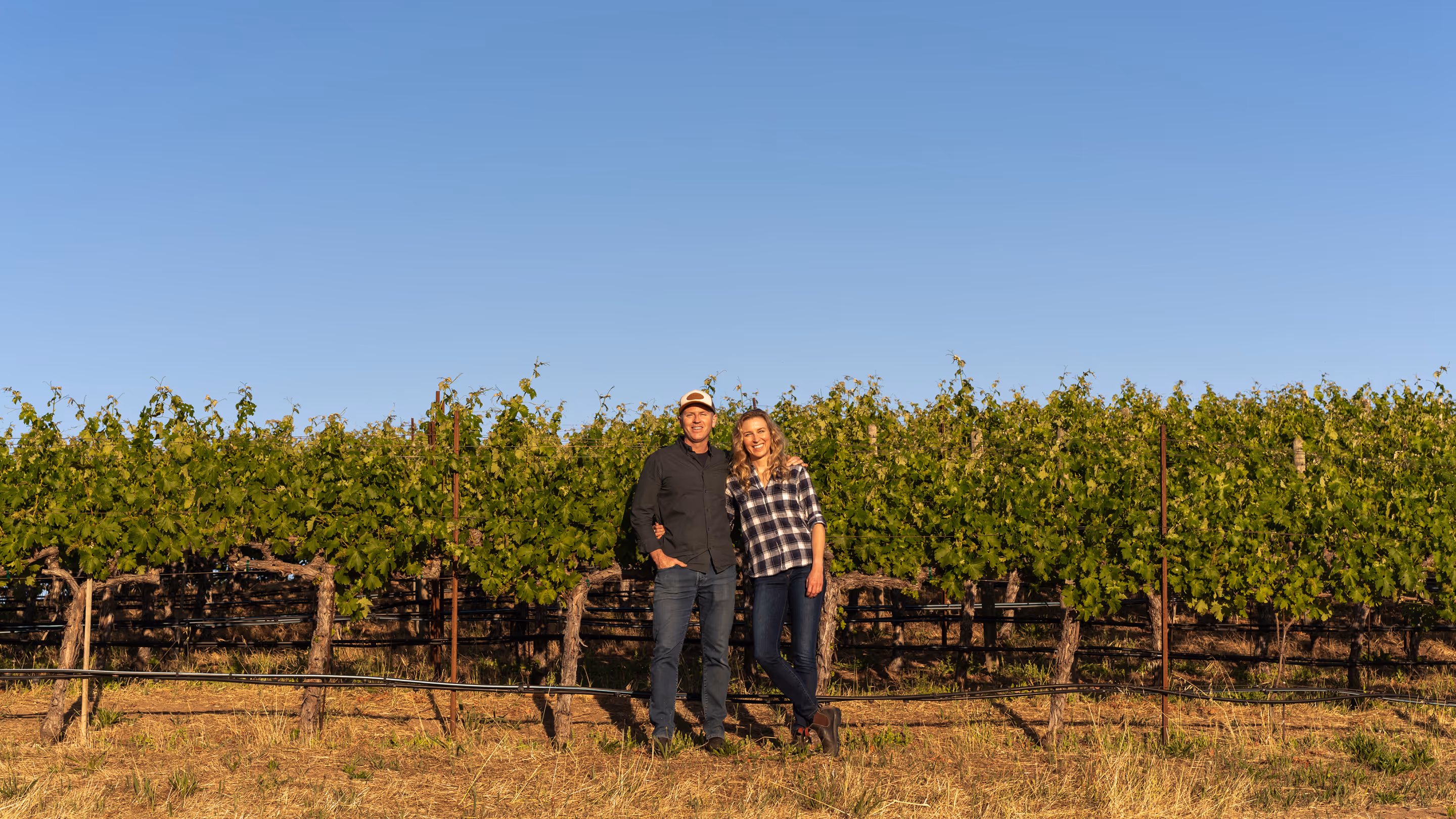Mike and Schatzi in front of a Husic vineyard row at golden hour.