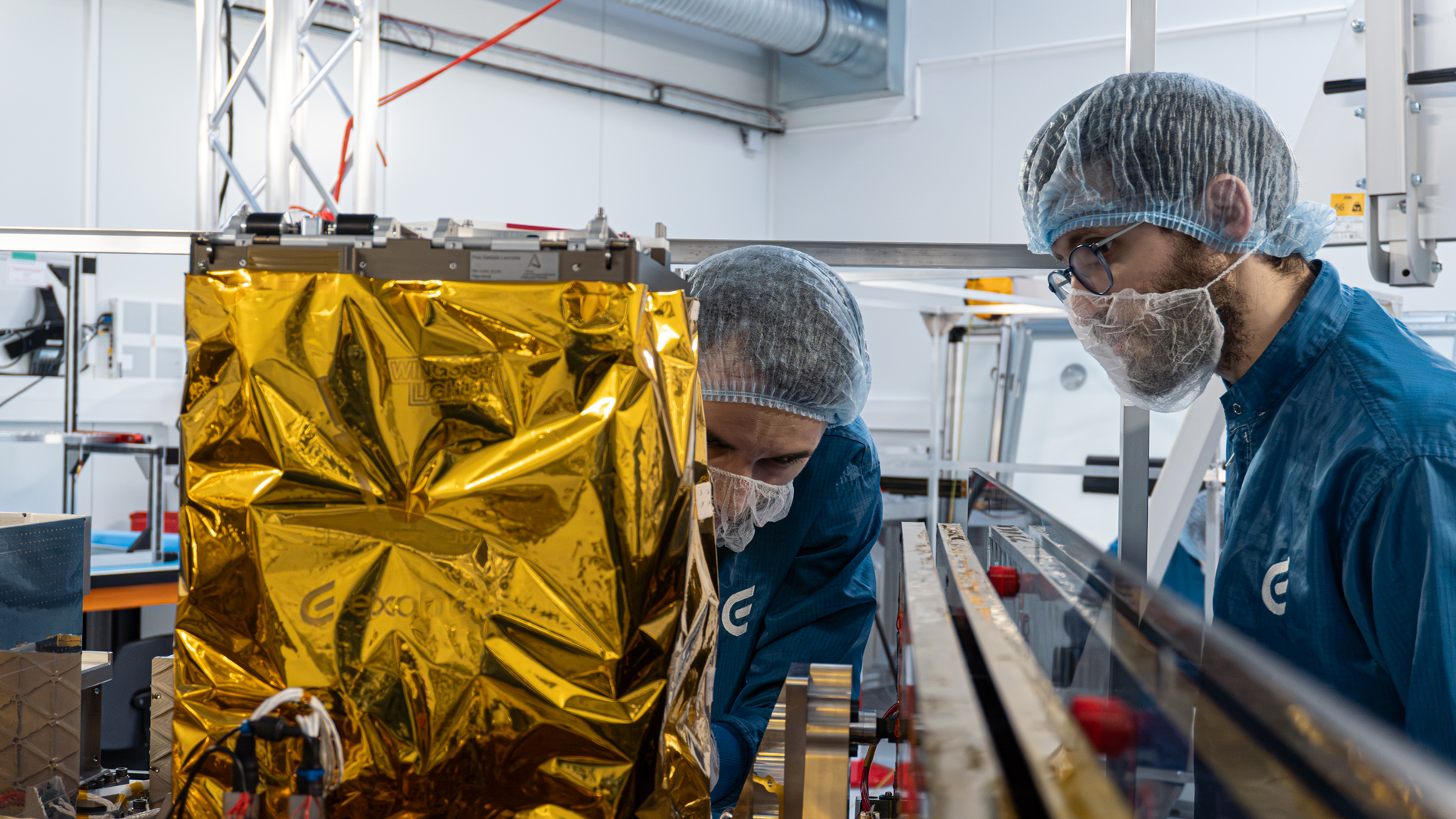 Scientist in blue protective clothing and hairnet working on a complex scientific instrument in a laboratory.