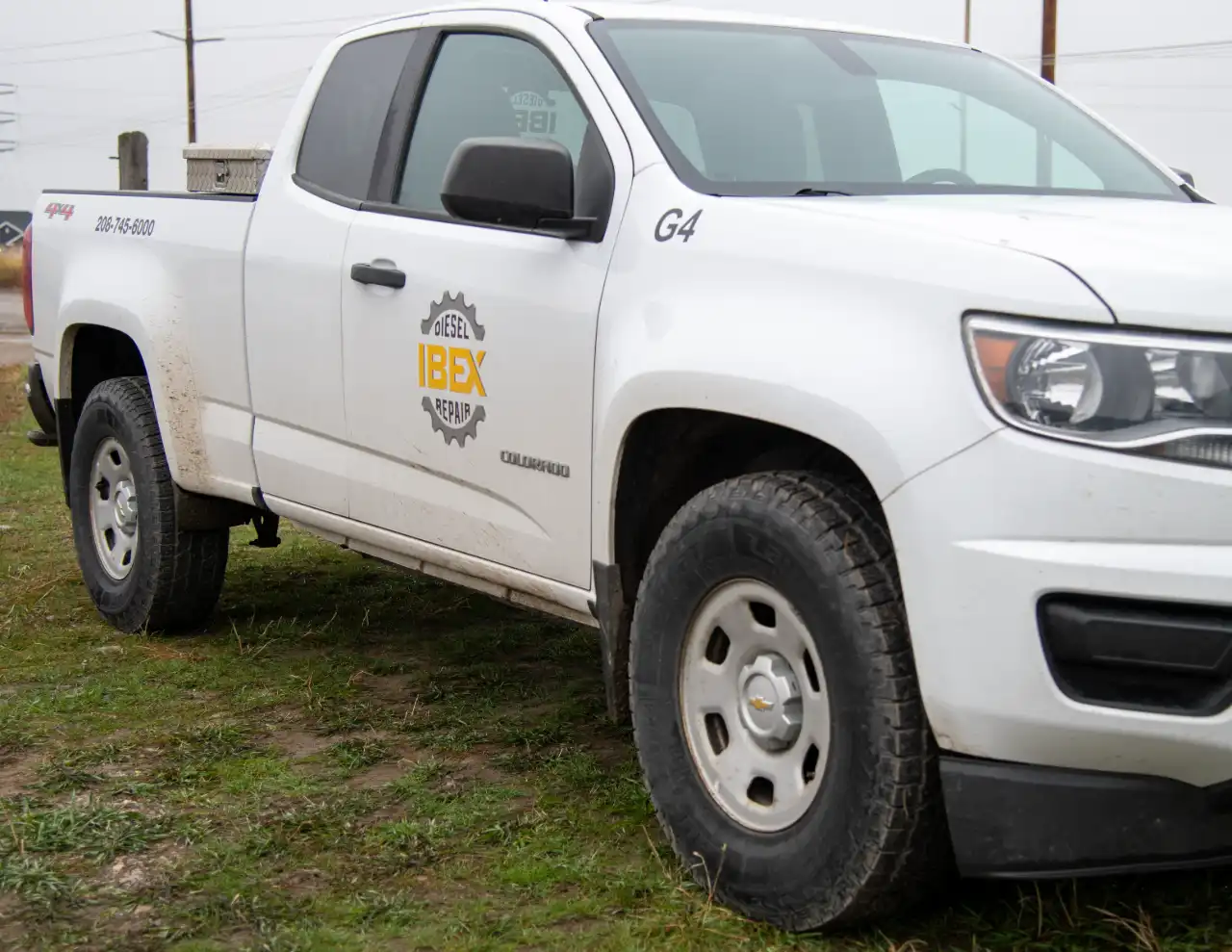 IBEX Diesel Repair service truck, mud-splashed Chevy Colorado 4×4 parked on wet grass at remote fleet site.