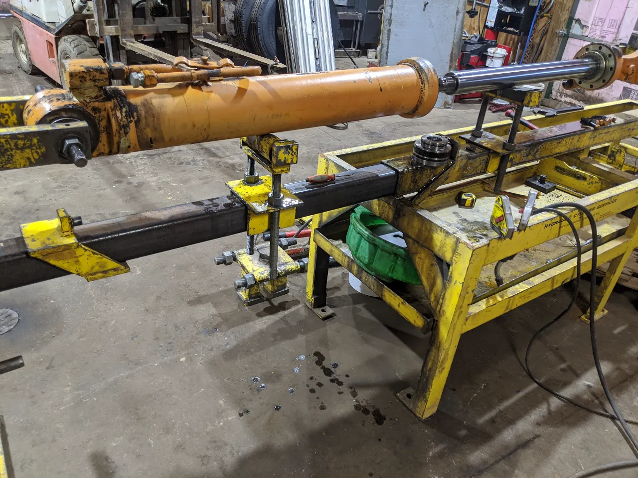 Hydraulic cylinder secured in a yellow repair bench with tools and clamps for heavy-duty maintenance.