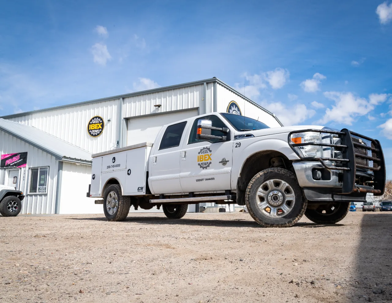 Diesel repair service truck parked outside IBEX Diesel Repair shop with visible logo and contact number.