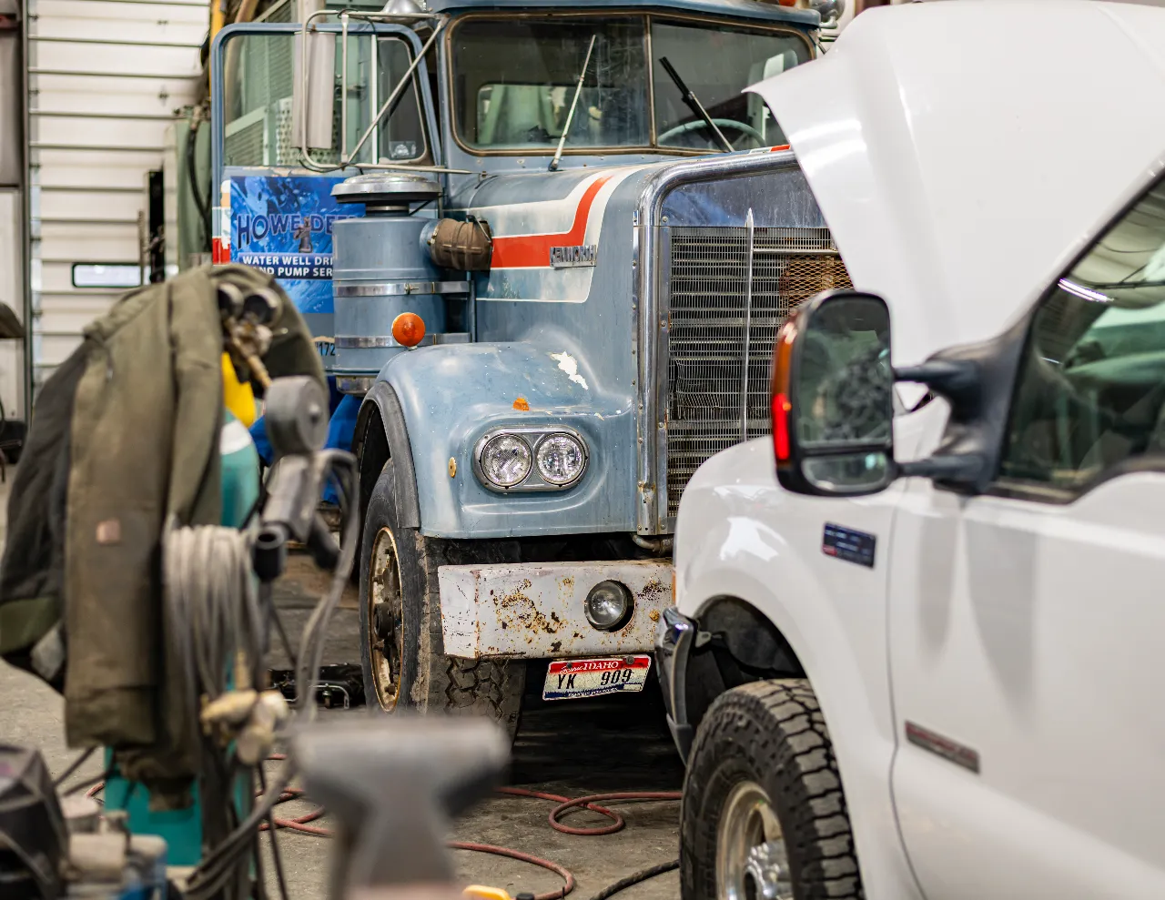 Fleet service in progress with a vintage blue semi-truck and a white service truck inside a repair bay.