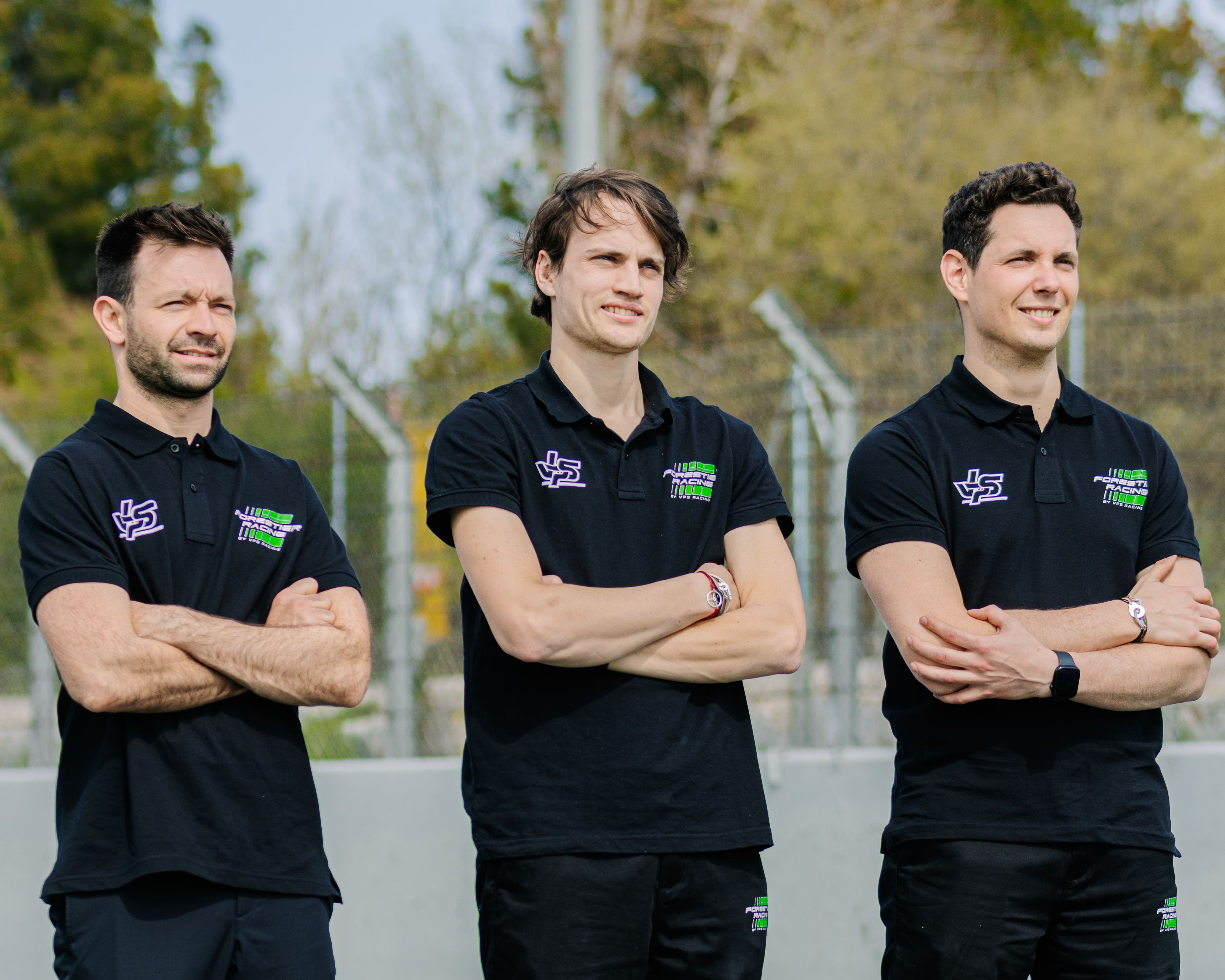 Three men wearing black polo shirts with racing logos standing outdoors with arms crossed.