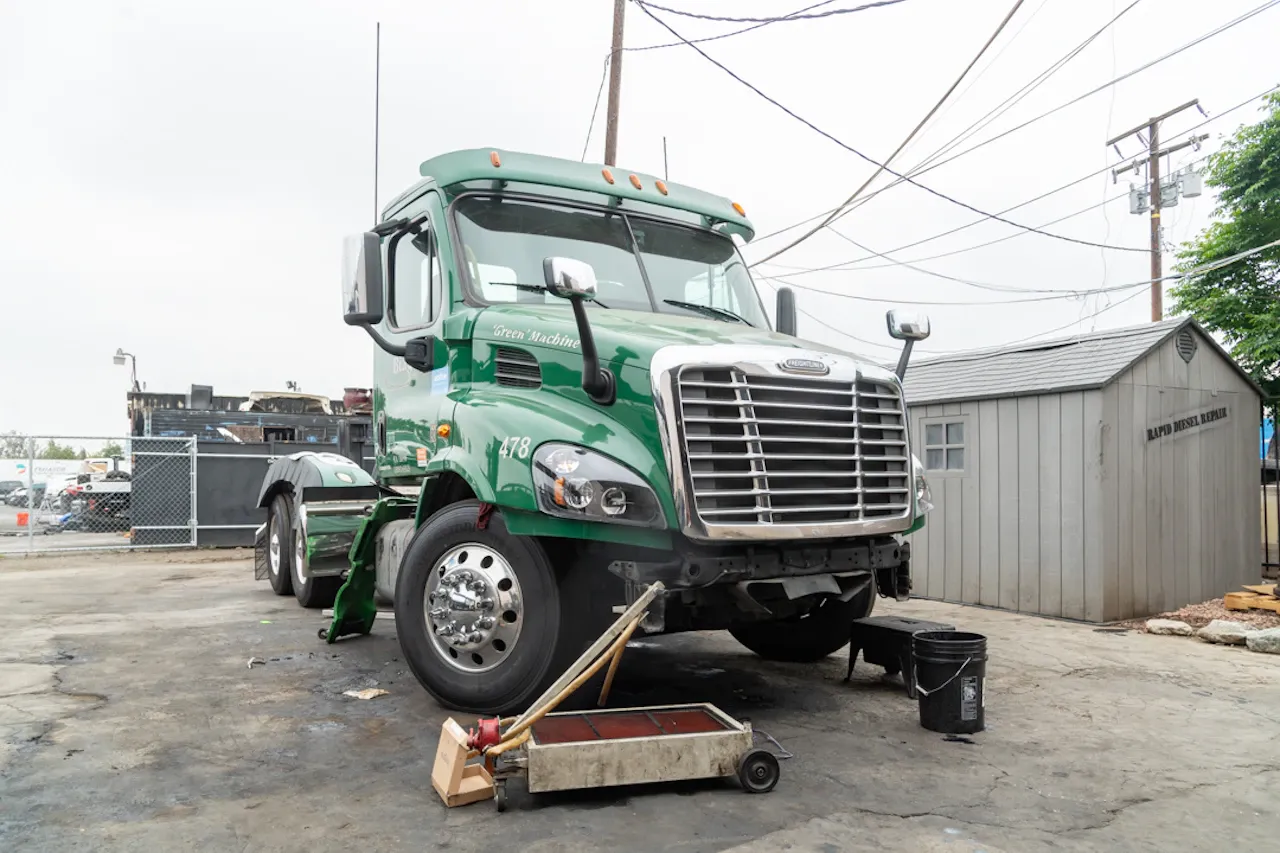 Preventive maintenance on a heavy-duty semi-truck with an oil drain pan positioned beneath the engine for fluid service and inspection.