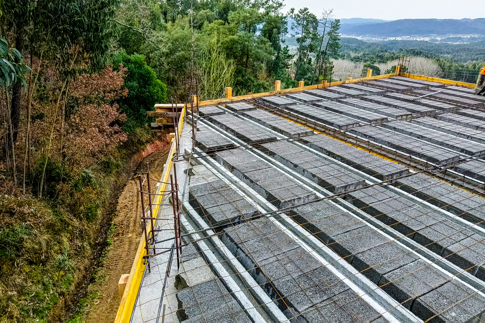 Estrutura de construção com blocos de concreto e armação de ferro, rodeada por árvores e natureza.