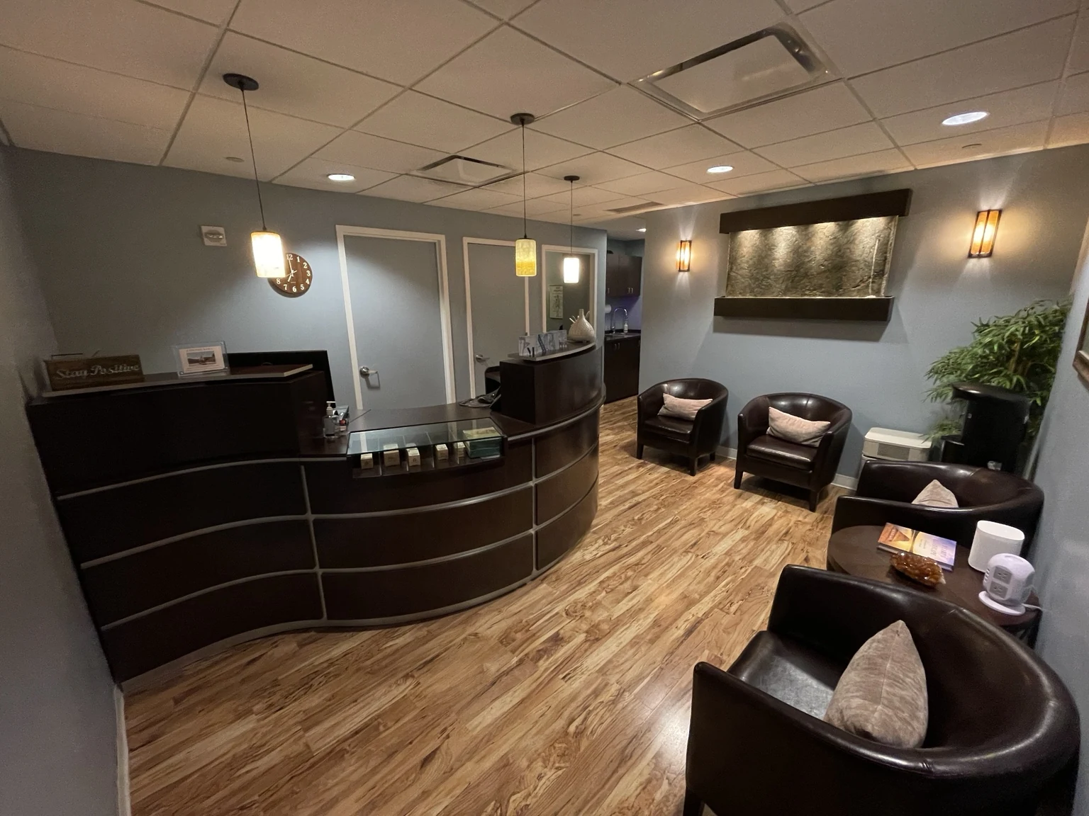 Body in Balance reception with a curved wood desk, soft lighting, comfortable seating, and a large wall fountain