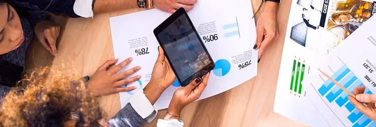 People around table looking at tablet and reports